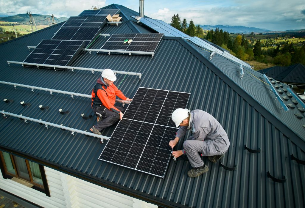Technicians installing photovoltaic solar panels on roof of house.